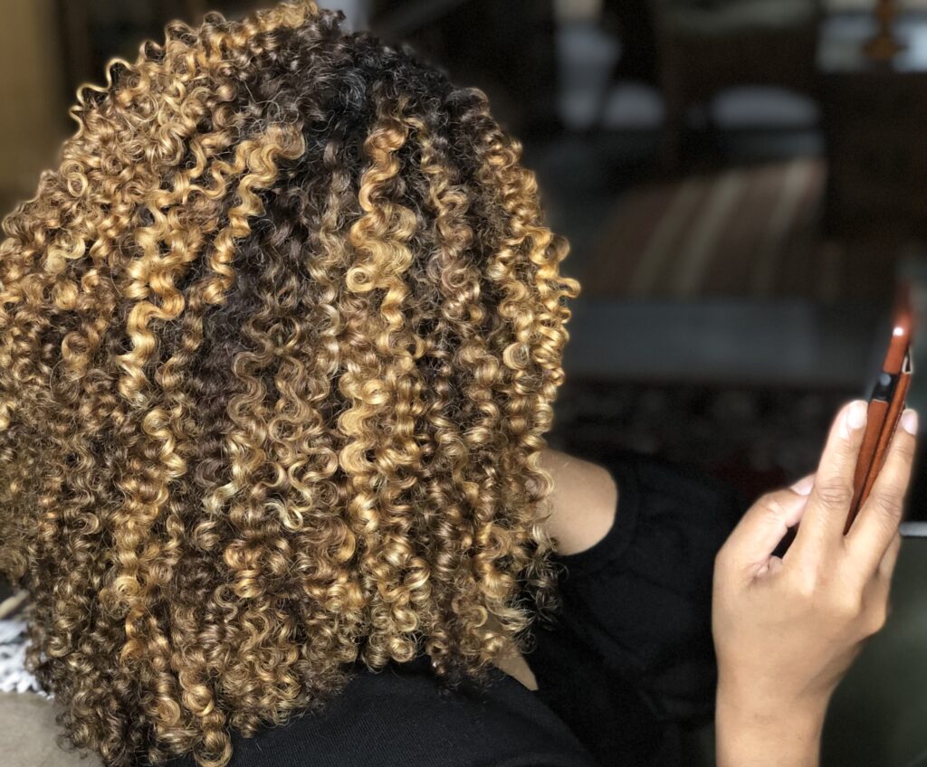 Side view of Verna's curly hair showing dark uncolored hair at the crown and bleached blonde curls through the lengths.