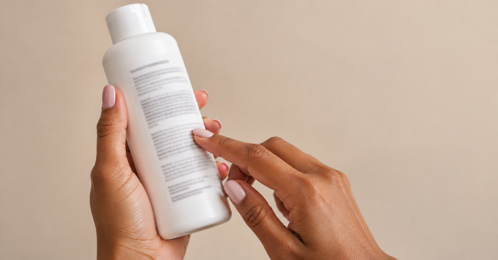 Hands holding a hair product bottle turned to show the ingredient list on the back label.